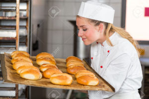 Baker or apprentice in bakery smelling fresh pastry, bread and buns